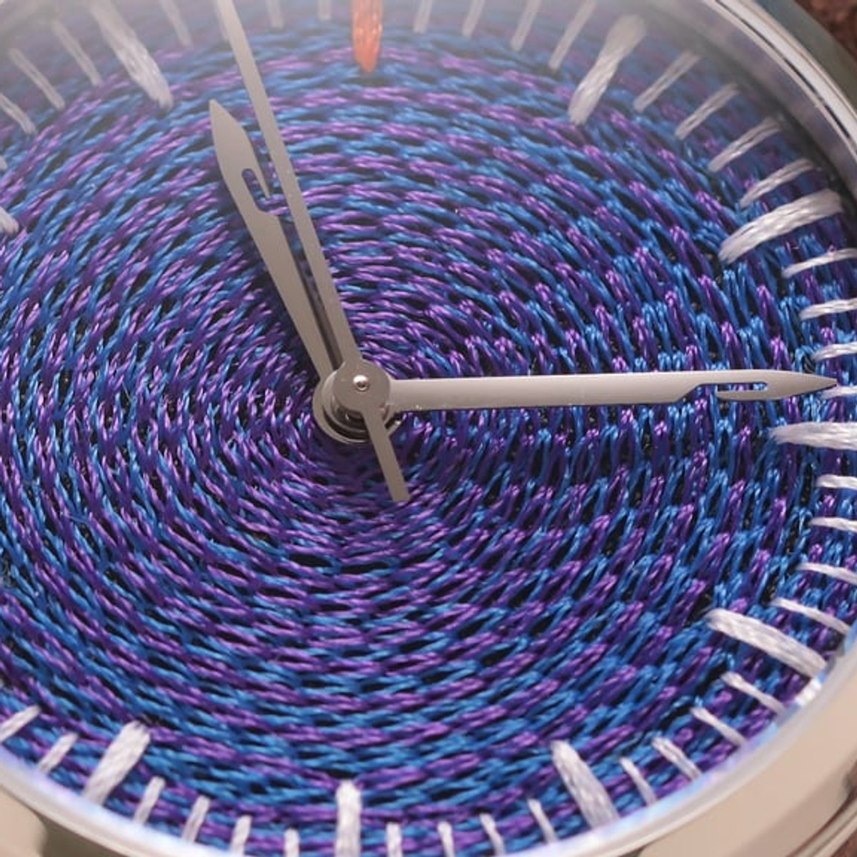 Extreme macro of the CORNELY dial: a spiral of raised blue and violet chenille loops, needle-shaped steel hands across it