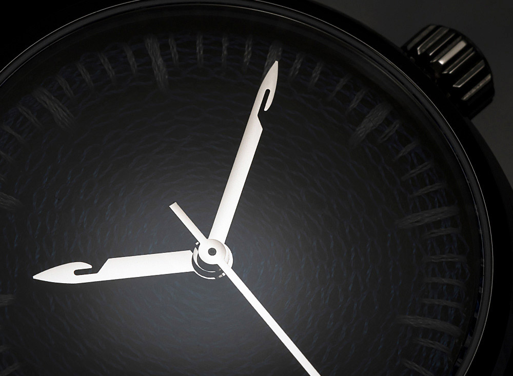 CORNELY watch face-on in near-black shadow, charcoal chenille dial, steel case and crown