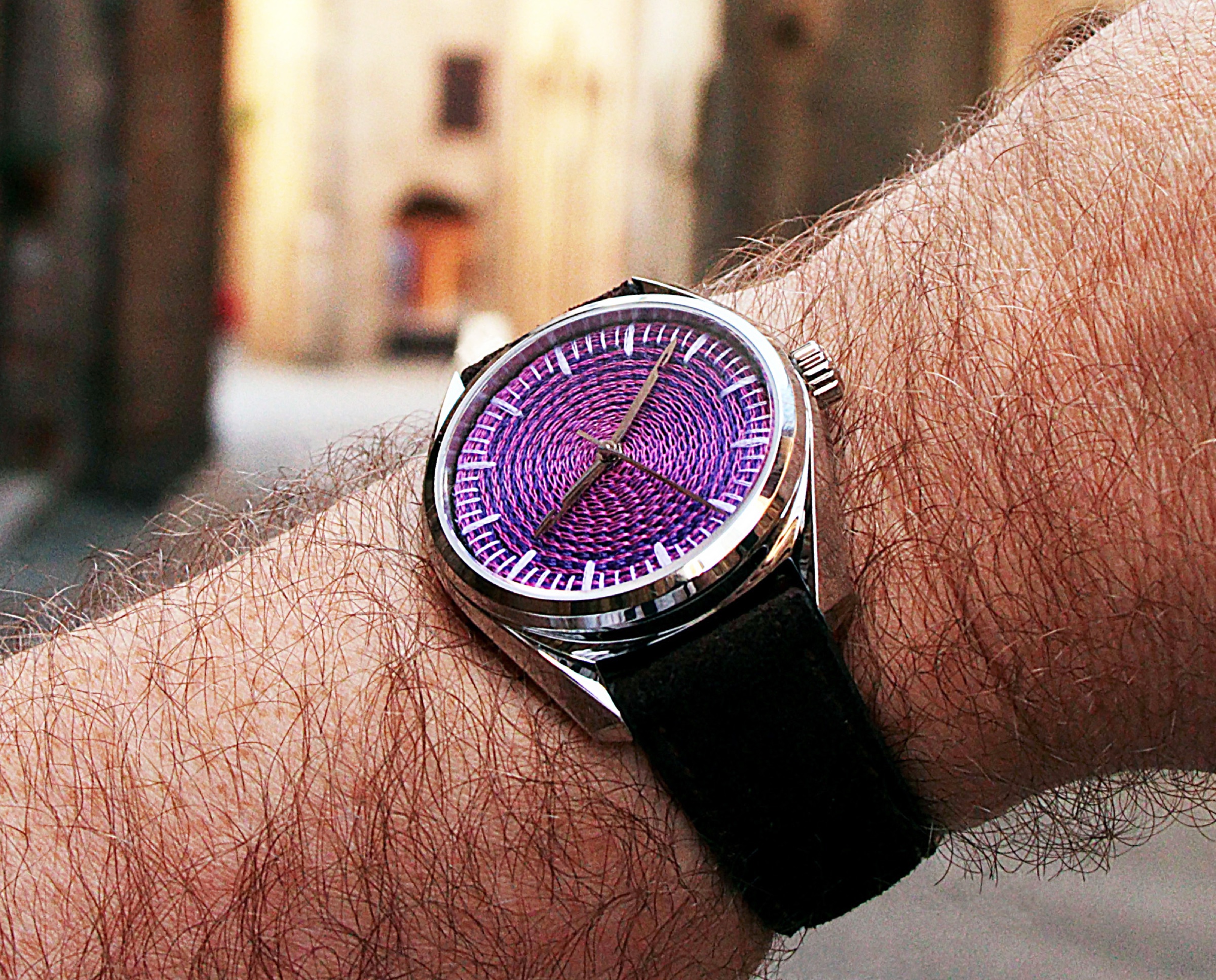 Watch worn on a wrist in natural outdoor light, pink-violet chenille dial